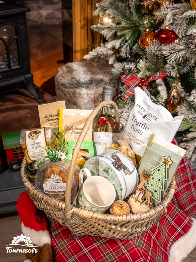 Panier garni avec vins, chocolats et douceurs devant un sapin de Noël.